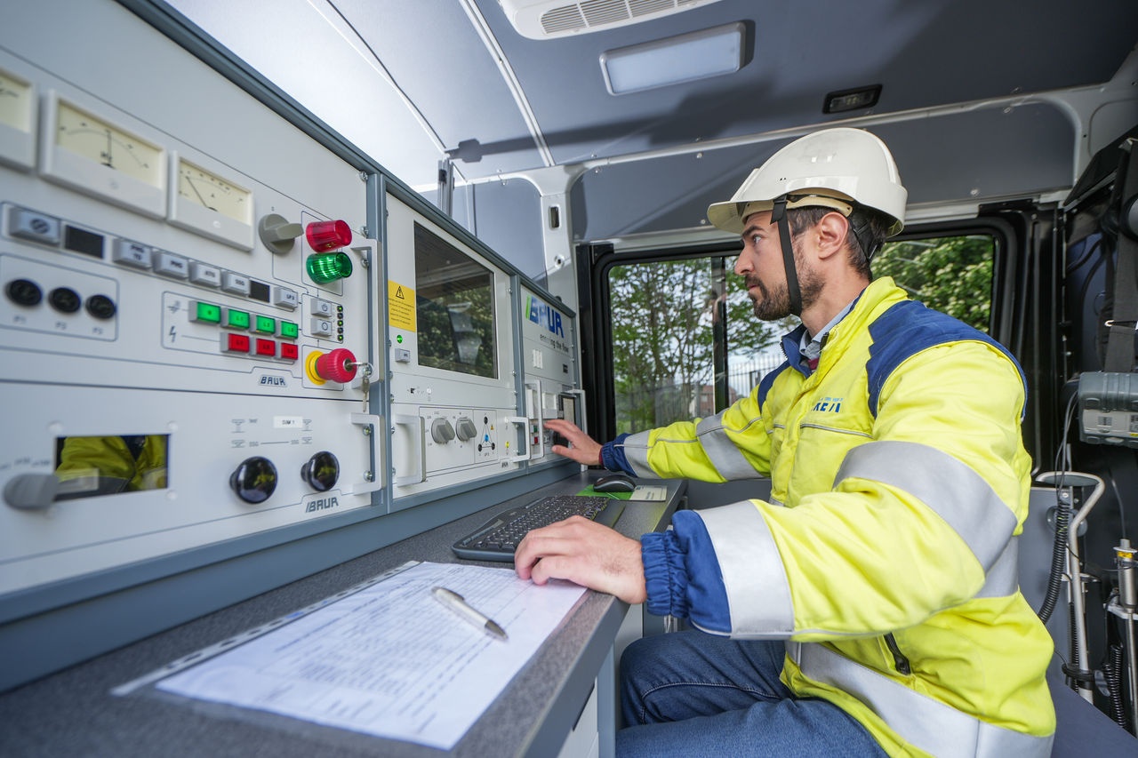 un lavoratore con gillet giallo catarifrangente e caschetto bianco che controlla un terminale elettrico